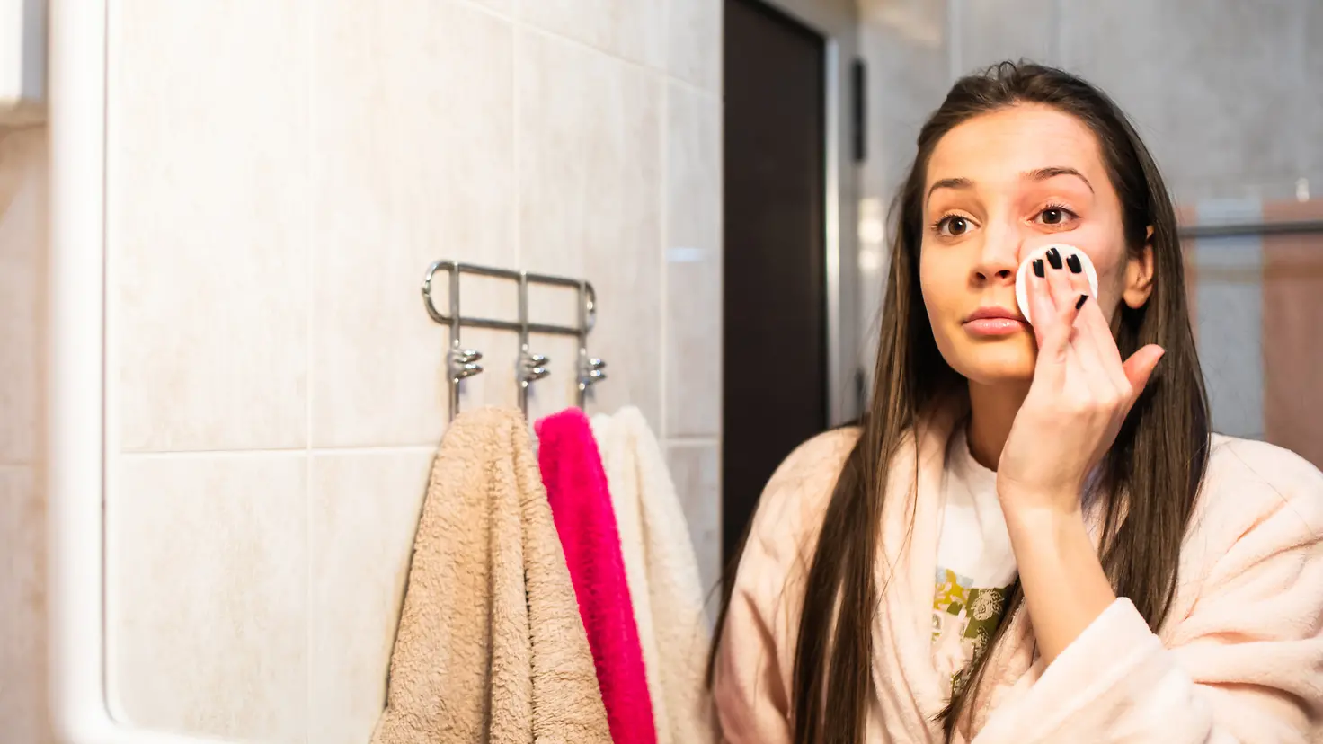 Eine junge Frau schminkt sich vor ihrem Badezimmerspiegel ab um einem Gerstenkorn vorzubeugen
