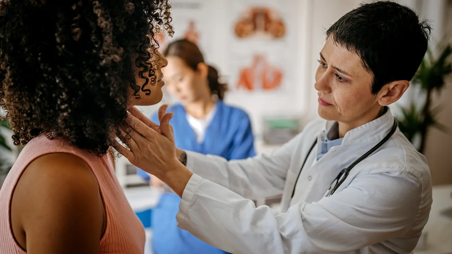 Eine Ärztin tastet den Hals einer Patientin ab, um die Größe der Schilddrüse festzustellen. Ist sie vergrößert, kann das ein Symptom einer Schilddrüsenüberfunktion sein.